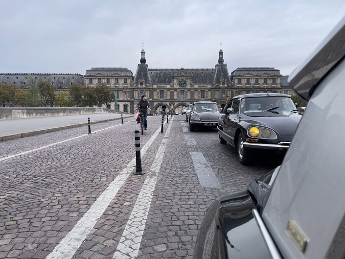 Les Citroën DS ont quitté le Louvre, roulant sur des pavés. Grâce à leur suspension hydropneumatique et leurs sièges moelleux, elles en isolent leur passagers.