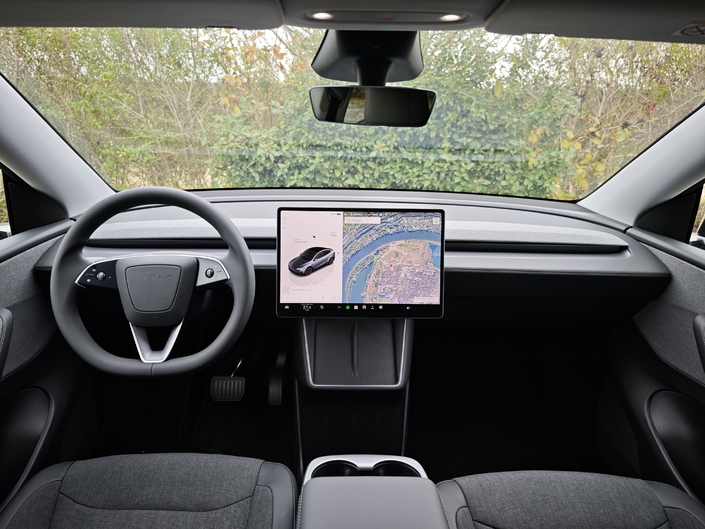 L’habitacle est toujours aussi sobre et dépouillé. La qualité de finition n’est pas dégradée par rapport aux autres Model Y, mais la sellerie est en tissu et les rangements de console centrale fermés sont remplacés par un bas de rangement ouvert au plancher.